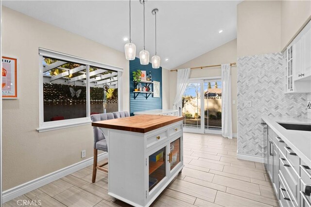 kitchen featuring white cabinetry, sink, hanging light fixtures, butcher block countertops, and a breakfast bar area