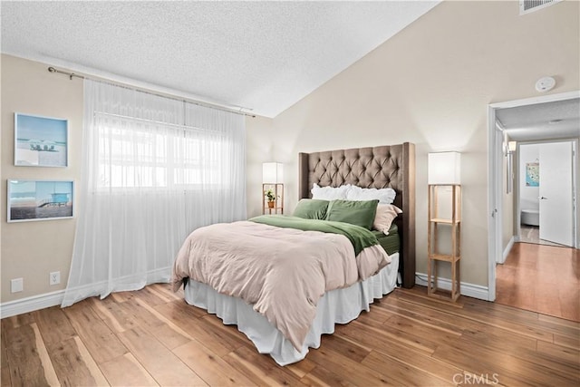 bedroom with vaulted ceiling, a textured ceiling, and hardwood / wood-style flooring