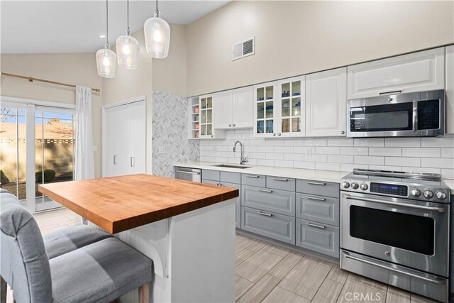 kitchen with a kitchen island, sink, white cabinetry, stainless steel appliances, and high vaulted ceiling