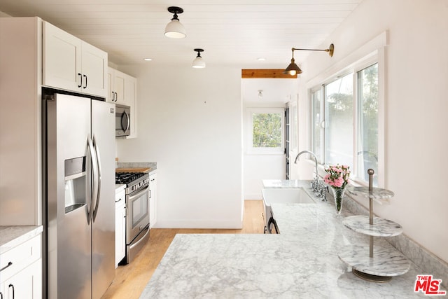 kitchen with stainless steel appliances, white cabinets, light stone countertops, light hardwood / wood-style flooring, and sink