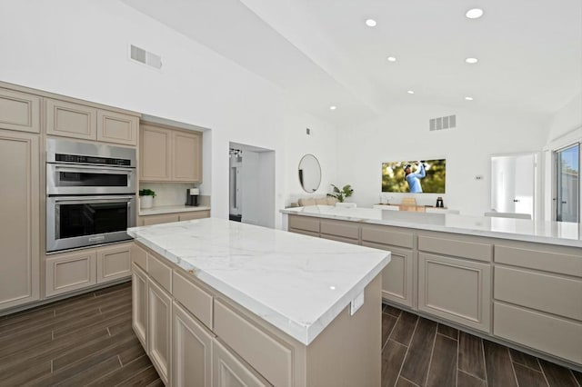 kitchen featuring light stone countertops, cream cabinets, vaulted ceiling, a kitchen island, and stainless steel double oven