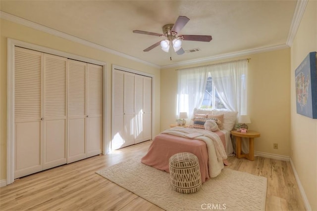 bedroom with multiple closets, ceiling fan, crown molding, and light hardwood / wood-style flooring