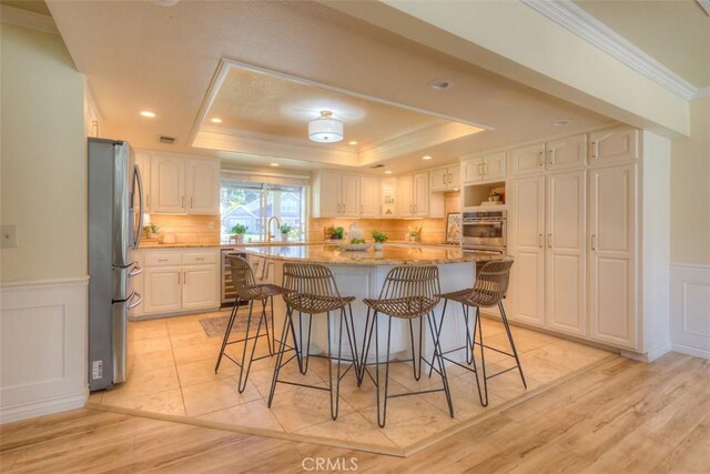 kitchen with stainless steel appliances, a tray ceiling, light stone countertops, and a kitchen island