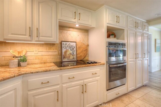 kitchen with light stone counters, backsplash, stainless steel double oven, and white cabinetry