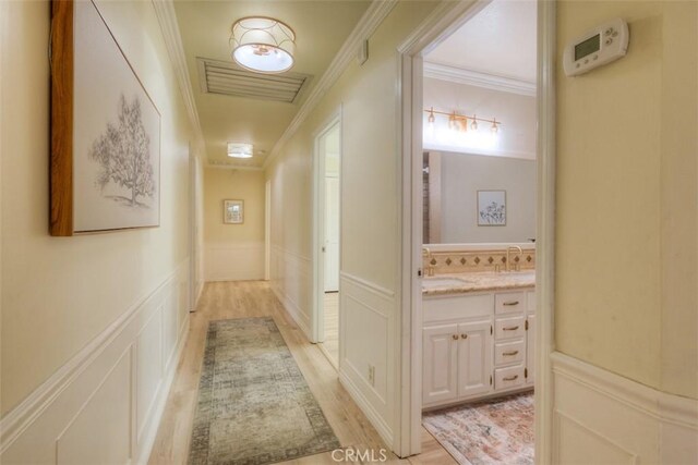 corridor featuring visible vents, wainscoting, crown molding, and a decorative wall