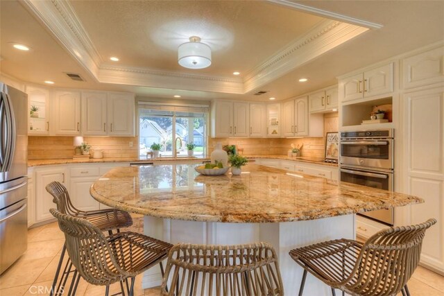 kitchen featuring light stone countertops, a raised ceiling, white cabinets, and a center island