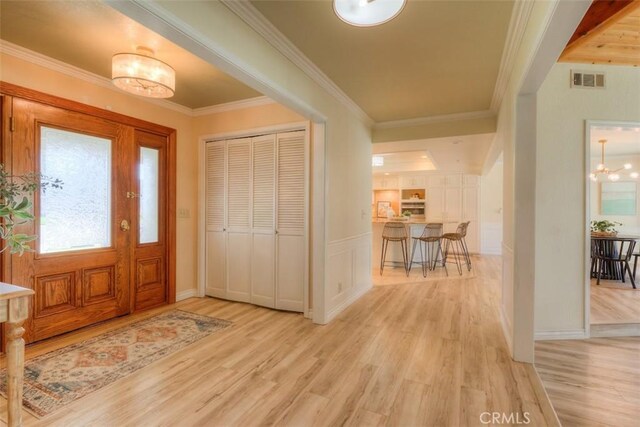 entryway with a chandelier, visible vents, ornamental molding, and light wood finished floors