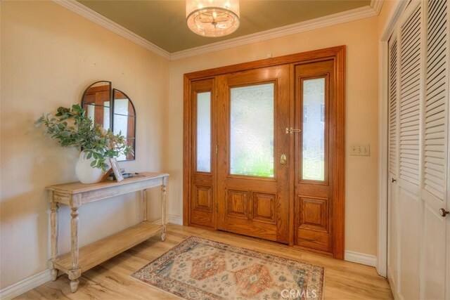 entrance foyer featuring baseboards, a chandelier, ornamental molding, and light wood-style floors