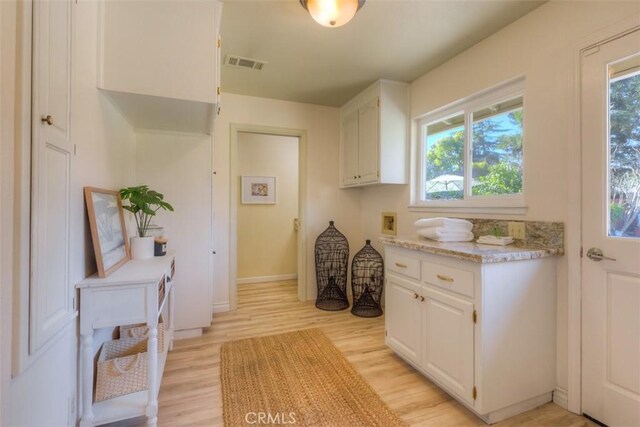 interior space featuring light wood-style flooring, light stone countertops, white cabinetry, and visible vents