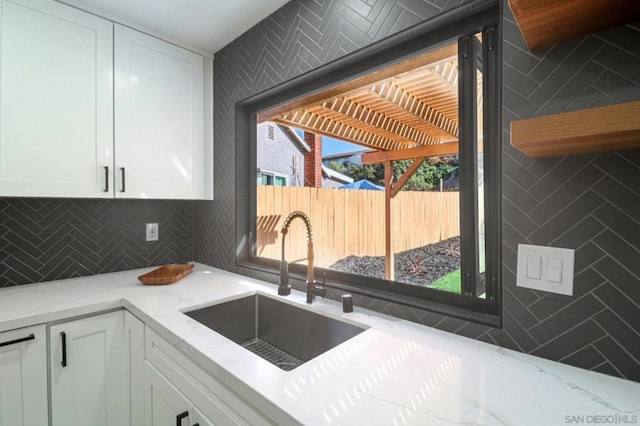 kitchen with white cabinets, light stone countertops, decorative backsplash, and sink