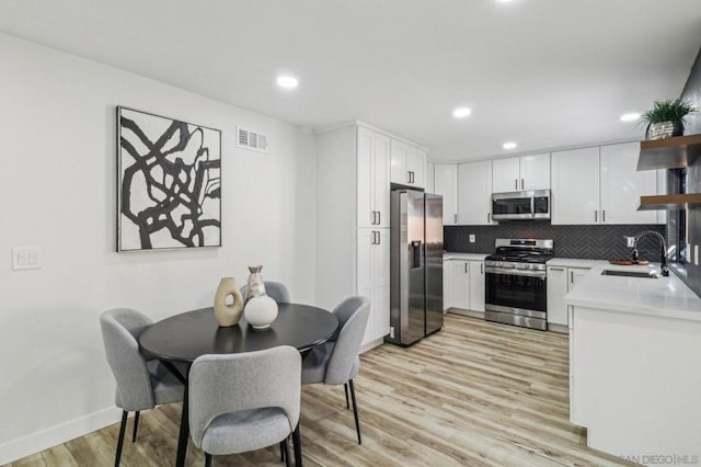 kitchen with light hardwood / wood-style floors, backsplash, white cabinetry, appliances with stainless steel finishes, and sink