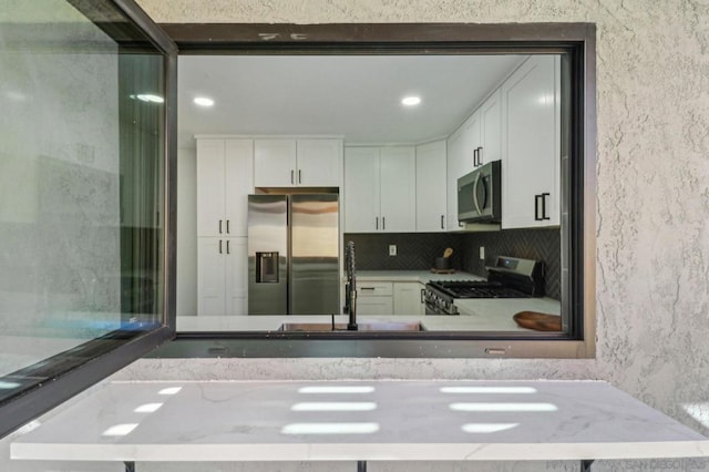 kitchen with sink, white cabinetry, tasteful backsplash, light stone countertops, and appliances with stainless steel finishes