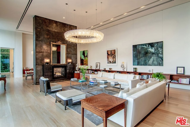 living room featuring light hardwood / wood-style flooring, an inviting chandelier, a multi sided fireplace, and a towering ceiling