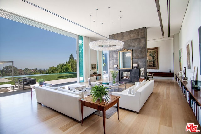 living room with a fireplace, an inviting chandelier, light hardwood / wood-style floors, and expansive windows