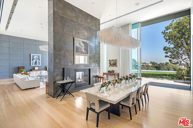 dining area featuring light hardwood / wood-style floors, a wall of windows, a fireplace, and a high ceiling