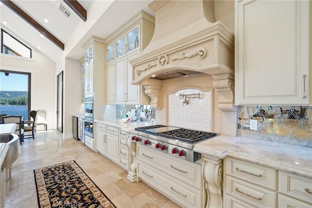 kitchen featuring custom exhaust hood, stainless steel gas cooktop, beamed ceiling, light stone counters, and decorative backsplash