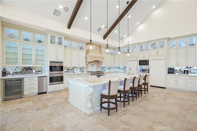 kitchen with built in appliances, tasteful backsplash, a large island with sink, beverage cooler, and hanging light fixtures