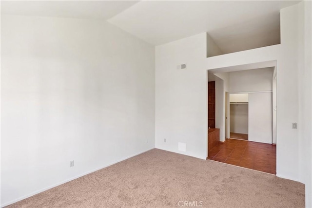 carpeted spare room featuring lofted ceiling and tile patterned flooring