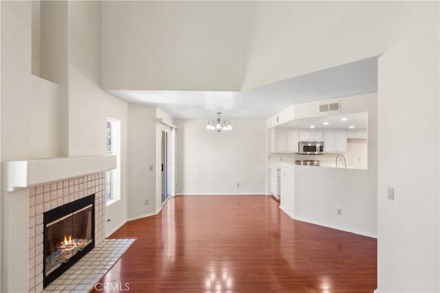 unfurnished living room featuring a chandelier, dark hardwood / wood-style floors, a high ceiling, a brick fireplace, and sink