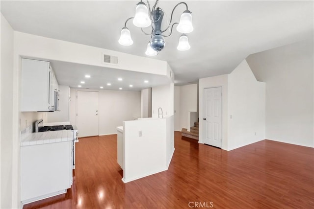 kitchen featuring dark hardwood / wood-style flooring, pendant lighting, gas range oven, white cabinetry, and an inviting chandelier