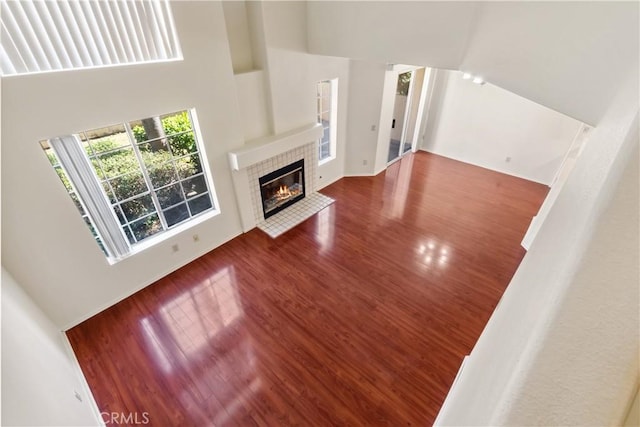 unfurnished living room with a tiled fireplace, wood finished floors, and a towering ceiling