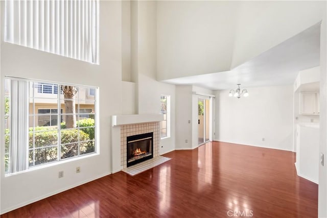 unfurnished living room with a towering ceiling, a tiled fireplace, hardwood / wood-style flooring, and a notable chandelier