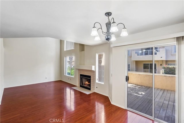 unfurnished living room featuring a tile fireplace, a notable chandelier, baseboards, and wood finished floors