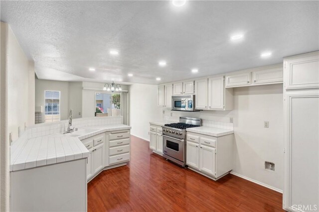 kitchen with stainless steel appliances, sink, white cabinets, kitchen peninsula, and dark hardwood / wood-style floors