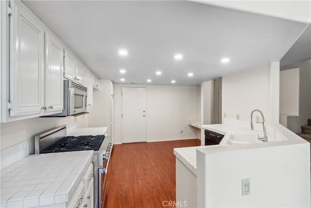 kitchen featuring tile countertops, stainless steel appliances, wood finished floors, a sink, and white cabinetry