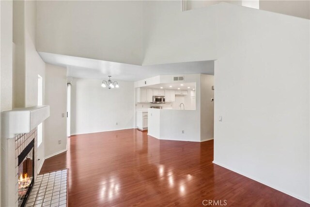 unfurnished living room with dark wood-type flooring, a high ceiling, a notable chandelier, a tiled fireplace, and sink