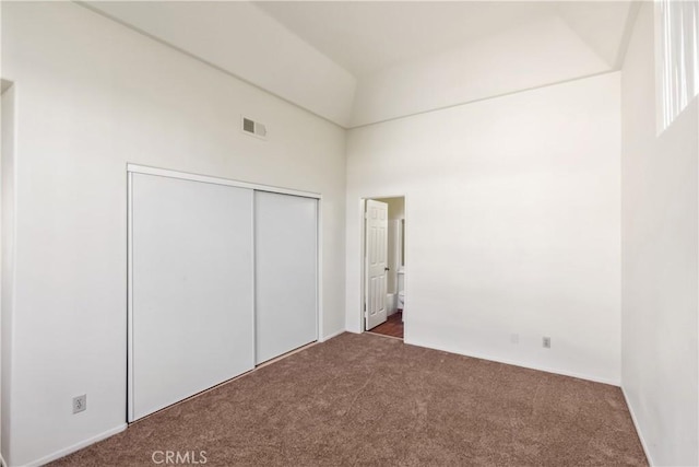 unfurnished bedroom featuring a closet, a towering ceiling, and dark colored carpet