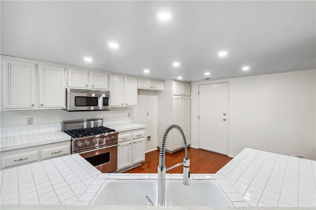 kitchen featuring tile countertops, stainless steel appliances, dark wood-style flooring, a sink, and white cabinetry