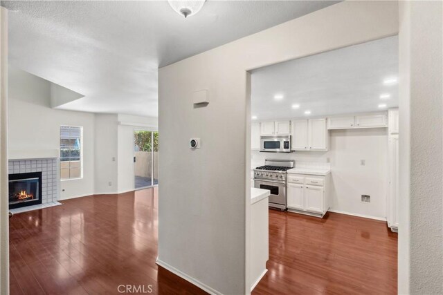 kitchen with stainless steel appliances, white cabinetry, dark hardwood / wood-style flooring, and a tile fireplace