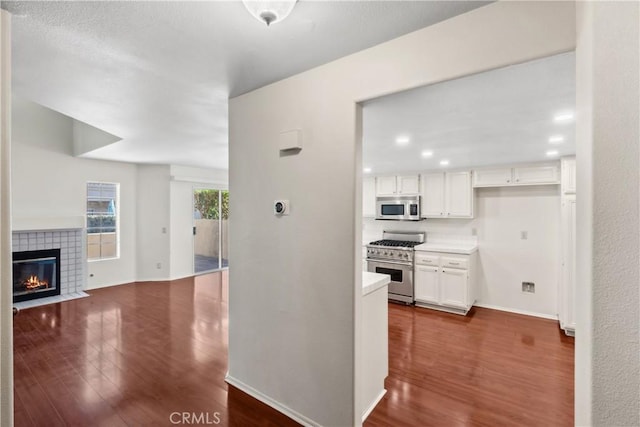 kitchen featuring white cabinets, stainless steel appliances, dark wood-type flooring, and a tile fireplace