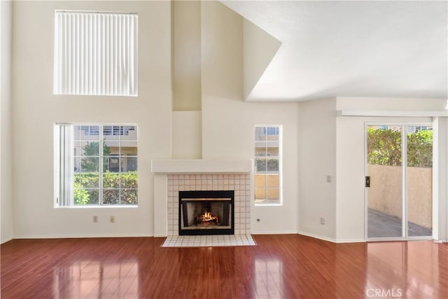 unfurnished living room with a towering ceiling, a tiled fireplace, and hardwood / wood-style floors