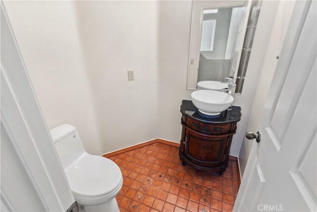 half bathroom featuring toilet, baseboards, and vanity