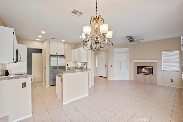 kitchen featuring stainless steel appliances, light tile patterned floors, ceiling fan with notable chandelier, white cabinets, and a fireplace