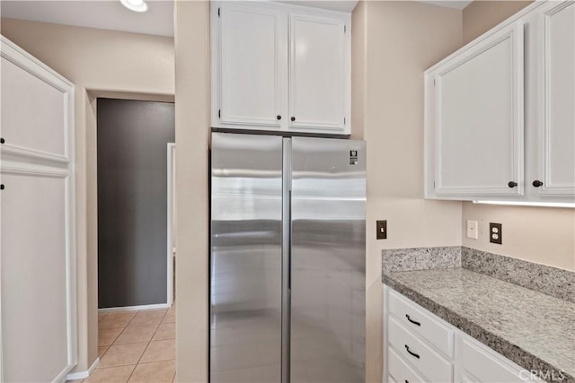 kitchen with white cabinets, stainless steel fridge, light stone countertops, and light tile patterned floors