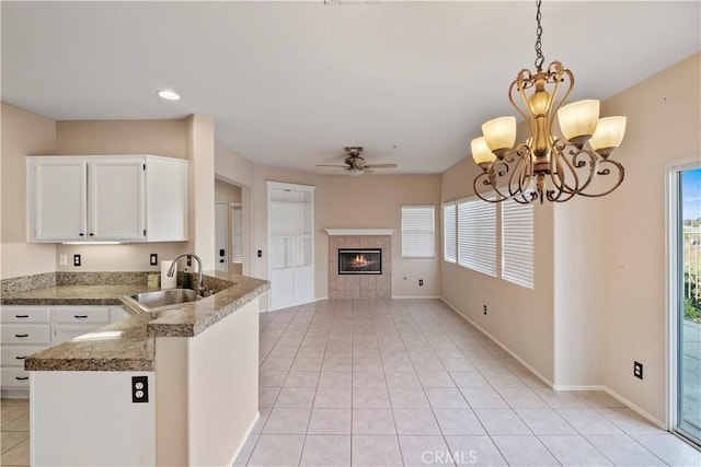 kitchen with a tiled fireplace, kitchen peninsula, sink, white cabinetry, and ceiling fan with notable chandelier