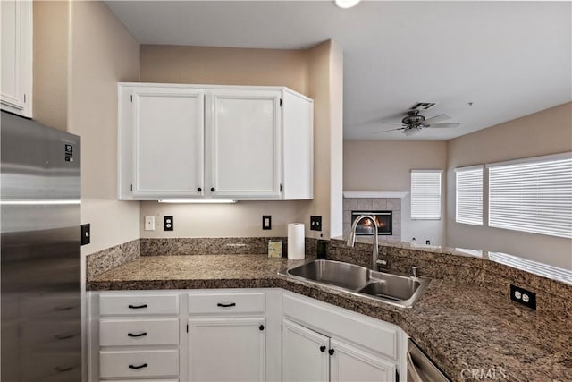 kitchen with sink, white cabinets, a tiled fireplace, ceiling fan, and stainless steel fridge