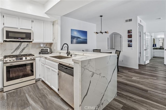 kitchen featuring light stone countertops, white cabinets, kitchen peninsula, backsplash, and stainless steel appliances