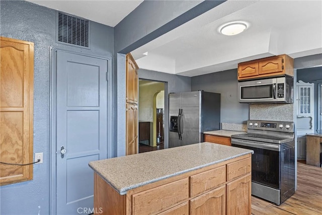 kitchen with backsplash, appliances with stainless steel finishes, a center island, and light wood-type flooring