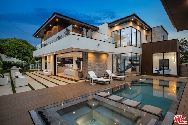 back house at dusk with a pool with hot tub, a balcony, and a patio area