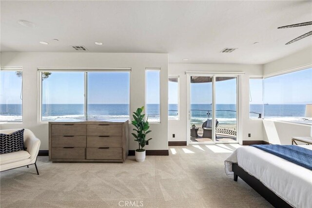 bedroom featuring multiple windows, access to exterior, light colored carpet, and a water view