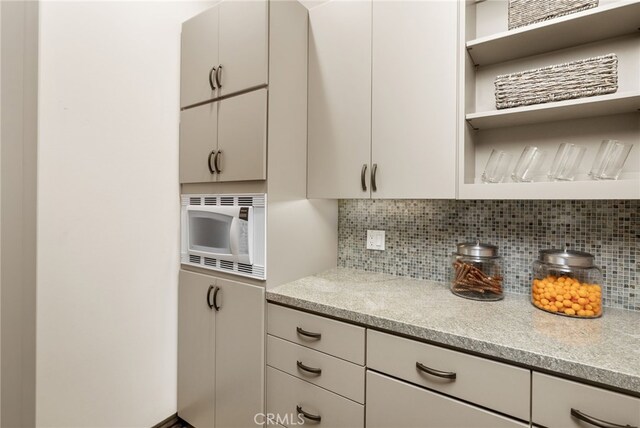 kitchen with tasteful backsplash, white microwave, and light stone countertops