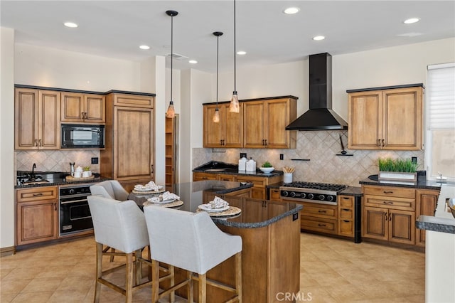 kitchen featuring black appliances, a center island, pendant lighting, wall chimney range hood, and backsplash