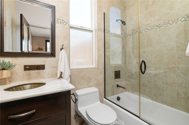 full bathroom featuring combined bath / shower with glass door, tile walls, decorative backsplash, vanity, and toilet