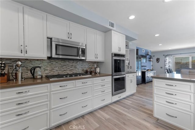 kitchen with backsplash, white cabinets, light hardwood / wood-style flooring, and stainless steel appliances