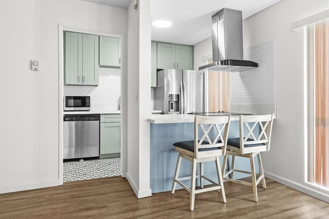 kitchen with green cabinets, a kitchen bar, tasteful backsplash, extractor fan, and appliances with stainless steel finishes