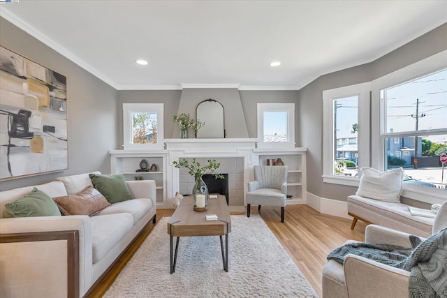 living room with ornamental molding, a tiled fireplace, and light hardwood / wood-style floors